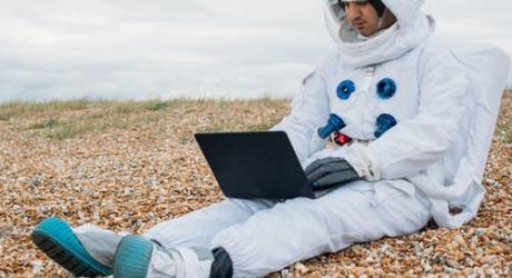 An astronaut sitting on a beach with a laptop