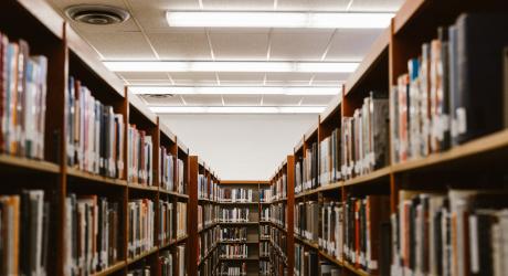 An alley in a library made of two rows of shelves, all filled with books.