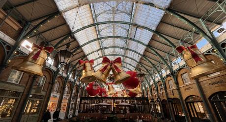 A view of Covent Garden at Christmas time with large golden bell and red ribbon decorations hanging from the rafters.