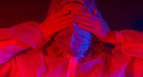 A person in PPE hiding their eyes behind their hands