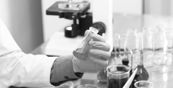 A close up of gloved hands in a lab holding a small beaker