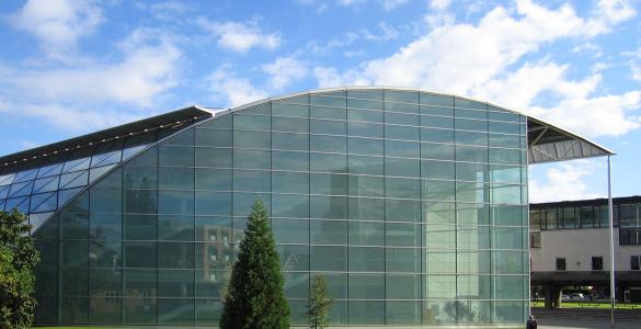 The Faculty of Law at the University of Cambridge, UK - a curved glass building on a bright green grass lawn under a blue sky.