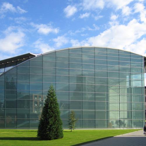 The Faculty of Law at the University of Cambridge, UK - a curved glass building on a bright green grass lawn under a blue sky.